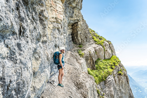Young woman on rocky hike trail under steep rock wall enjoys view on lake Walensee. Schnürliweg, Walensee, St. Gallen, Switzerland, Europe.
