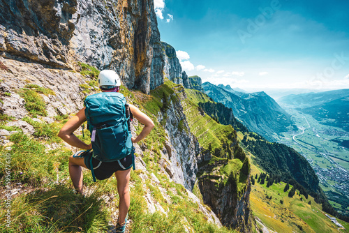 Athletic woman on steep rocky hike trail enjoys scenic view on Churfürsten mountain range at noon. Schnürliweg, Walensee, St. Gallen, Switzerland, Europe.