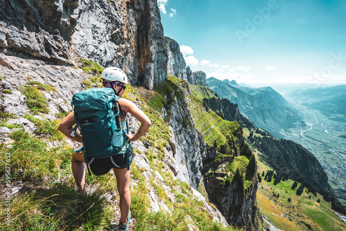 Athletic woman on steep rocky hike trail enjoys scenic view on Walenstadt with Churfürsten mountain range in the background. Schnürliweg, Walensee, St. Gallen, Switzerland, Europe.