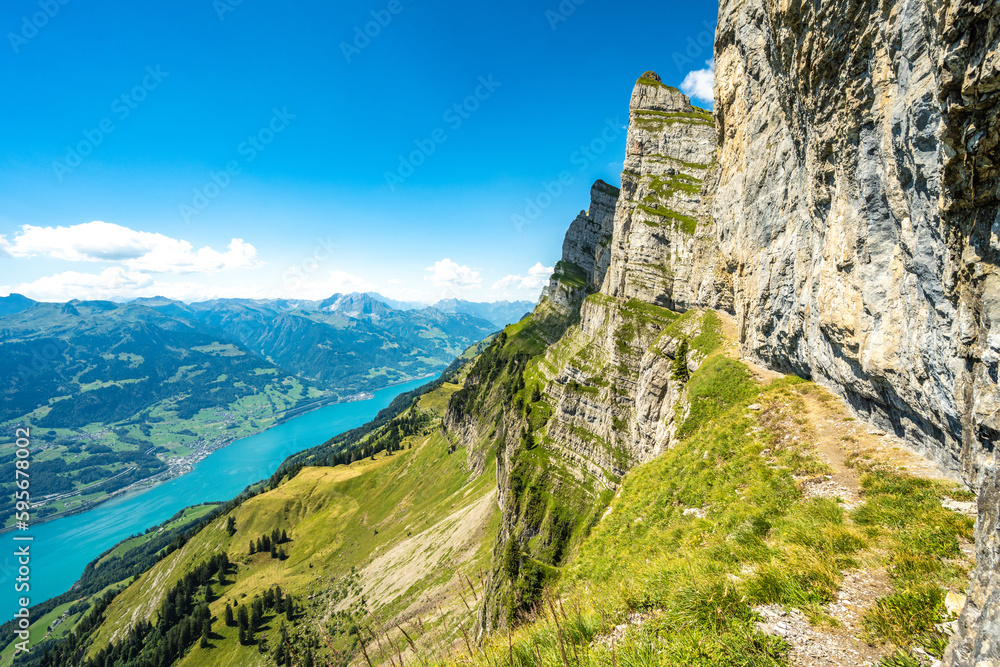 Hike trail under steep rock wall with scenic view on Walensee and Churfürsten mountain range in the background. Schnürliweg, Walensee, St. Gallen, Switzerland, Europe.