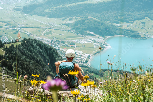 Athletic woman on a rock next to the hiking trail and enjoys the view of lake Walensee and Walenstadt.  Schnürliweg, Walensee, St. Gallen, Switzerland, Europe. photo