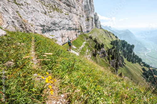 Athletic woman stands on rock below steep rock wall and enjoys view into the valley. Schnürliweg, Walensee, St. Gallen, Switzerland, Europe. photo