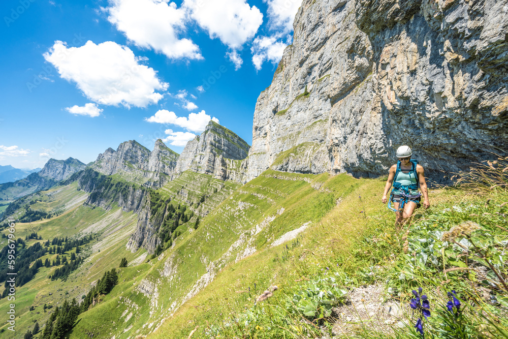Mountaineer hiking on flowery meadow below steep rock wall with scenic view on the Churfürsten mountain range. Schnürliweg, Walensee, St. Gallen, Switzerland, Europe.