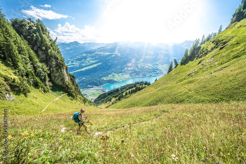 Sporty woman walks on a path through a steep meadow with a panoramic view of lake Walensee and the Swiss Alps. Schnürliweg, Walensee, St. Gallen, Switzerland, Europe. photo