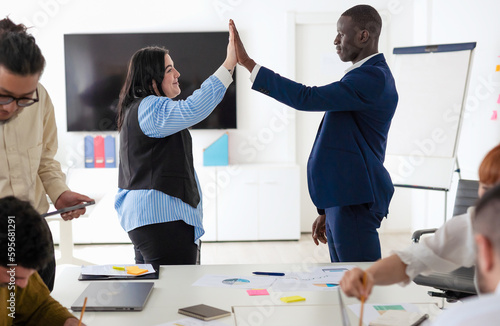Caucasian woman and African man colleagues high five during a meeting in boardroom. Celebration of success, cooperation and inclusivity concept.