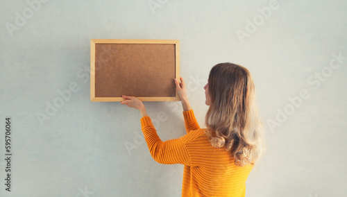 Foto Young woman decorating interior, hanging blank a photo frame mockup on white wal