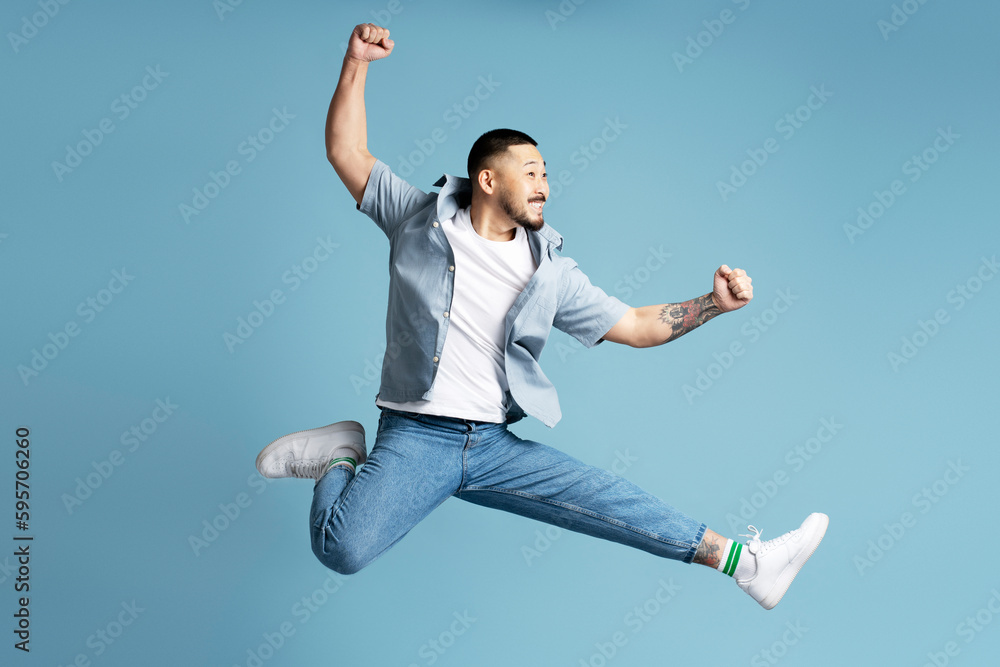 Happy emotional asian man wearing stylish casual clothes, white shoes running fast, jumping high isolated on blue background. Positive lifestyle concept Happy emotional asian man wearing stylish casual clothes, white shoes running fast, jumping high isolated on blue background. Positive lifestyle concept
