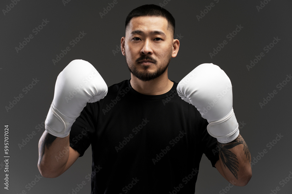 Portrait of serious handsome asian boxer wearing white boxing gloves looking at camera, isolated on black background. Sport competition, motivation concept Portrait of serious handsome asian boxer wearing white boxing gloves looking at camera, isolated on black background. Sport competition, motivation concept