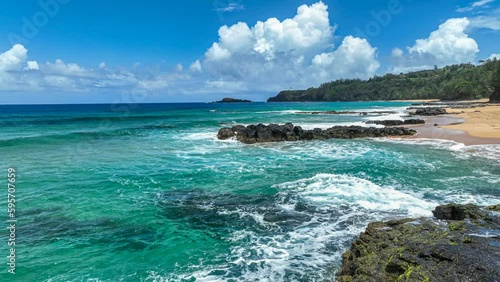 Flying over blue waters of the Pacific ocean as waves crash against a remote Hawaiian beach with black volcanic rock