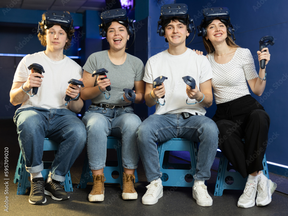 four smiling students with virtual reality devices sit and pose in gaming modern club. future technologies. digital interface