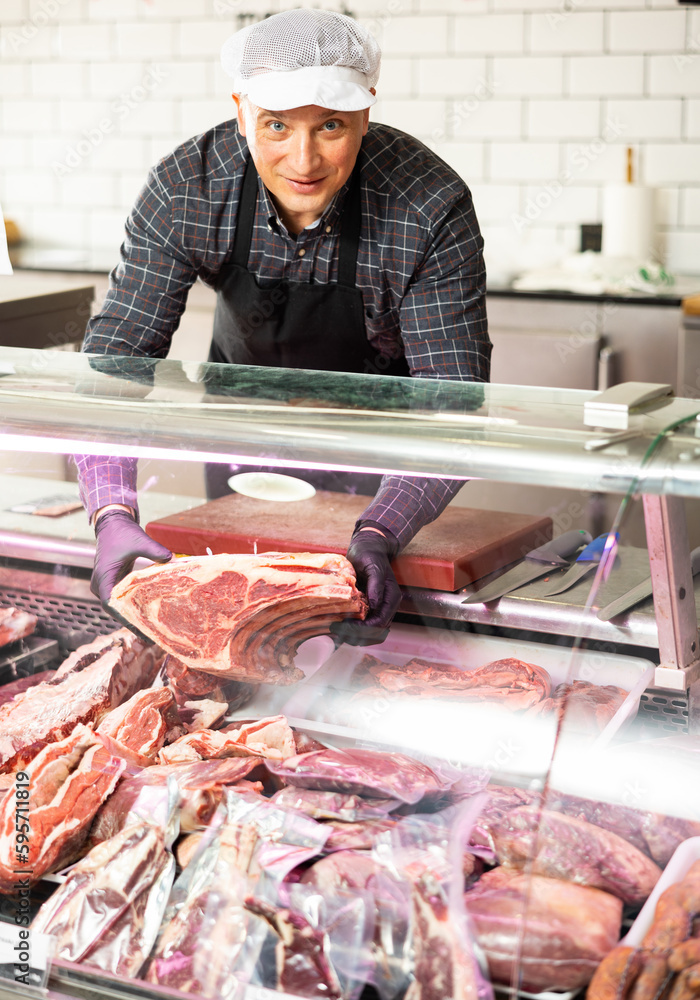 Diligent male butcher offering to sell big piece of beef beef in butcher shop