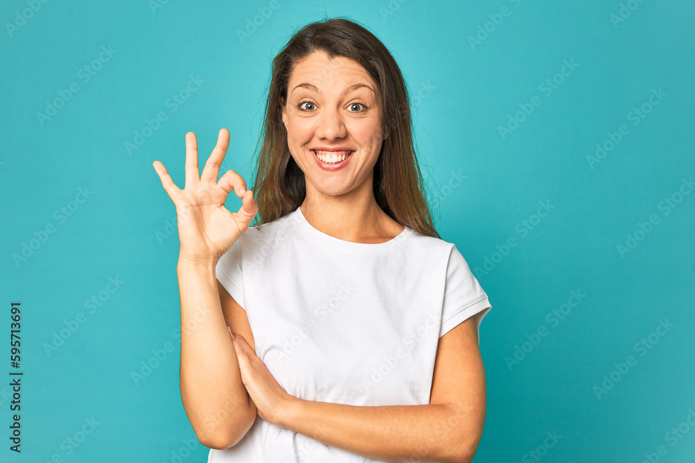 A young caucasian woman isolated winks an eye and holds an okay gesture with hand. A young caucasian woman isolated winks an eye and holds an okay gesture with hand.