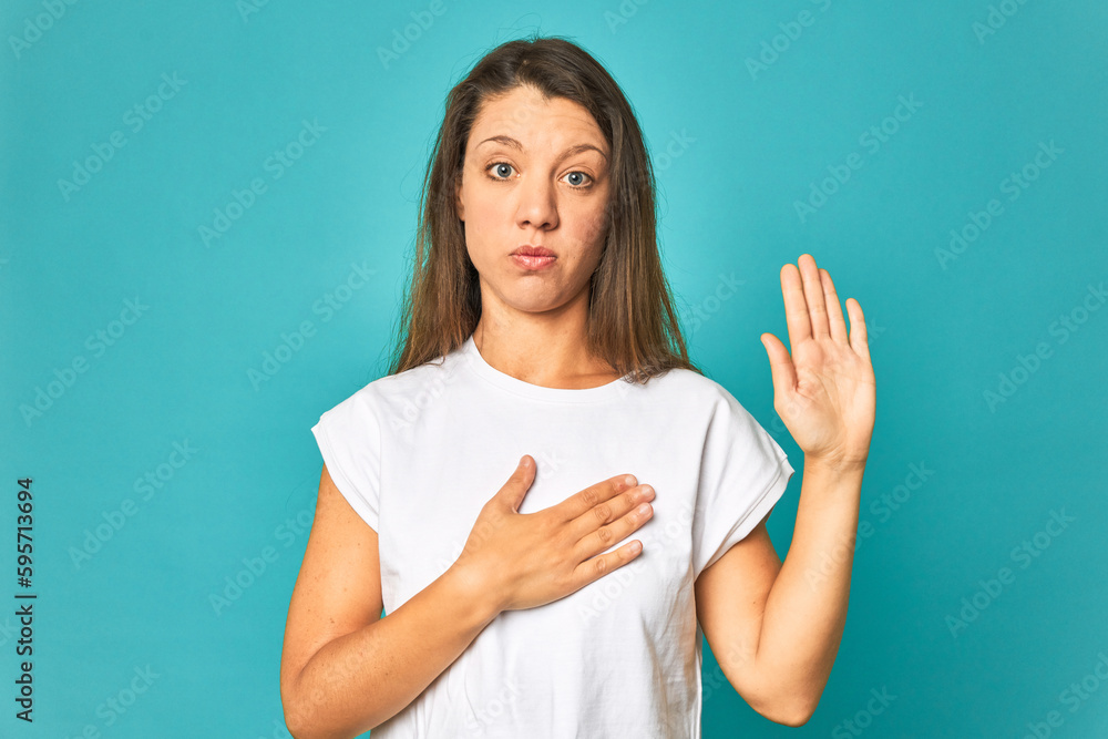 Fototapeta premium A young caucasian woman isolated taking an oath, putting hand on chest.