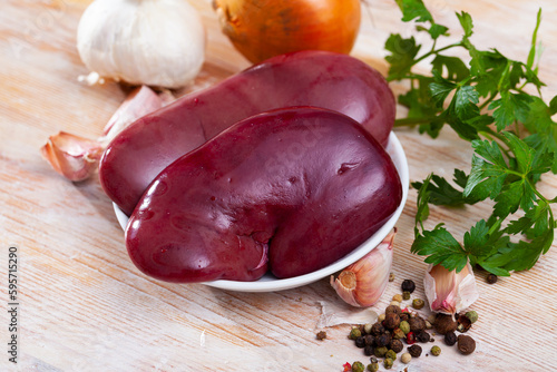 Raw pork kidneys ready for cooking with fresh vegetables, greens and spices on wooden surface photo