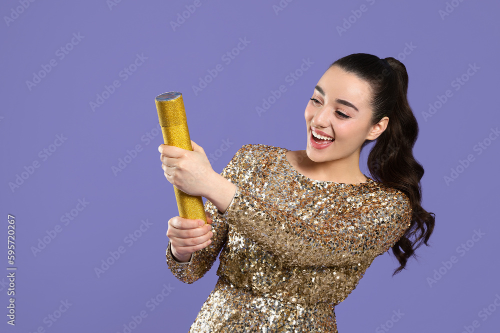 Young woman blowing up party popper on purple background, space for text Young woman blowing up party popper on purple background, space for text