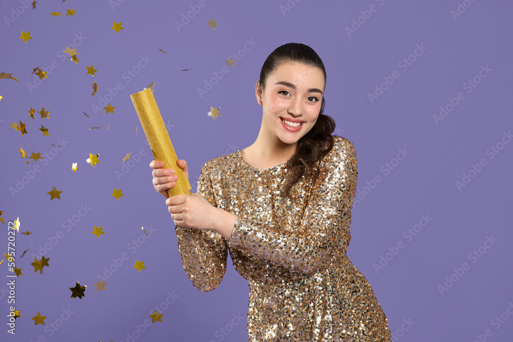 Young woman blowing up party popper on purple background Young woman blowing up party popper on purple background