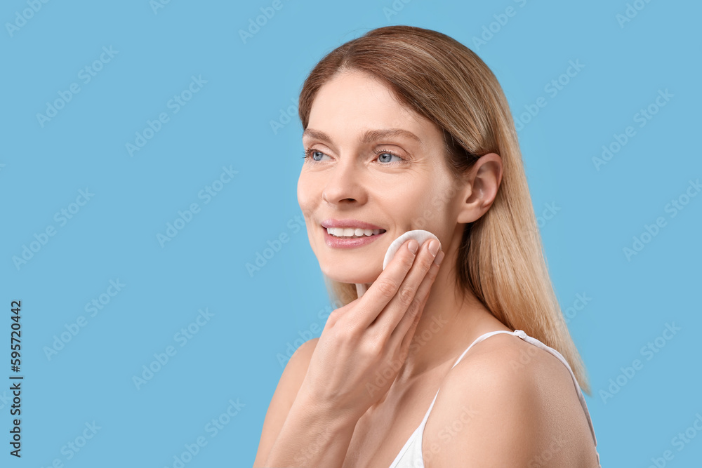 Beautiful woman removing makeup with cotton pad on light blue background, space for text Beautiful woman removing makeup with cotton pad on light blue background, space for text