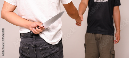 Two male shaking hand with one hand holding a knife on white background.Weak trust. Backstabbing friends.Man hold and hide knife at the back ready to kill.Blackmail and unreliable partnership concept. photo