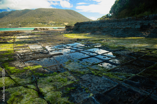 Tessellated pavement in Tasmania is a stunning place formed by patterned stilstone with the tasman sea in the background and a mountain. photo