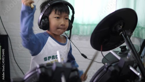 Asian child boy play electronic drum with headphone. Kid beat drumstick in hard rock music at home. Concept of music learning, happy relaxing time, freedom, little kid musician.