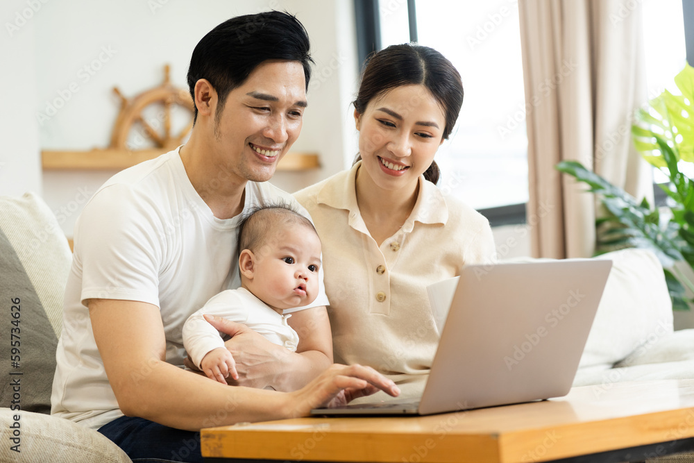 image of asian family with baby sitting on sofa using laptop image of asian family with baby sitting on sofa using laptop