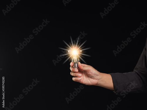 Close-up of hand holding a light bulb while standing on a black background