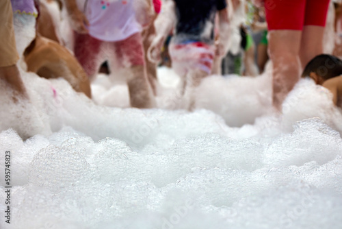 Foamy entertainment party, people are merrily floundering in the foam, catching soap bubbles. Cheerful people have fun at the holiday with soap bubbles
