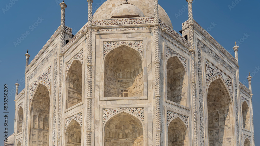 Beautiful white marble Taj Mahal against the blue sky. Symmetrical mausoleum with arches, domes, spires decorated with ornaments, inlays of precious stones. India. Agra.
