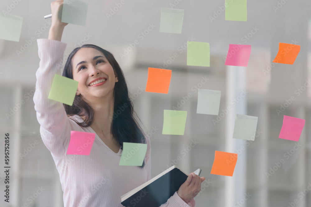 The concept of brainstorming is exemplified as a millennial Asian businesswoman shares ideas using Post-it notes, which she places on a glass wall. The concept of brainstorming is exemplified as a millennial Asian businesswoman shares ideas using Post-it notes, which she places on a glass wall.