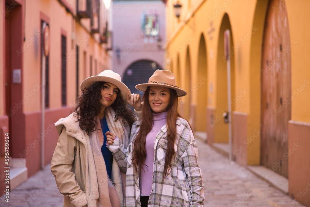 Two women, young and beautiful, wearing hats and coats, posing looking at the camera happy and relaxed. Concept beauty, fashion, autumn, winter, cold, friendship, couples.