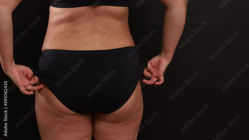 Back view of unrecognizable plus-size woman wearing black comfortable sportswear, adjusting trying on black seamless sports panties, stretching cloth on black background. Body positive, underwear. Back view of unrecognizable plus-size woman wearing black comfortable sportswear, adjusting trying on black seamless sports panties, stretching cloth on black background. Body positive, underwear.