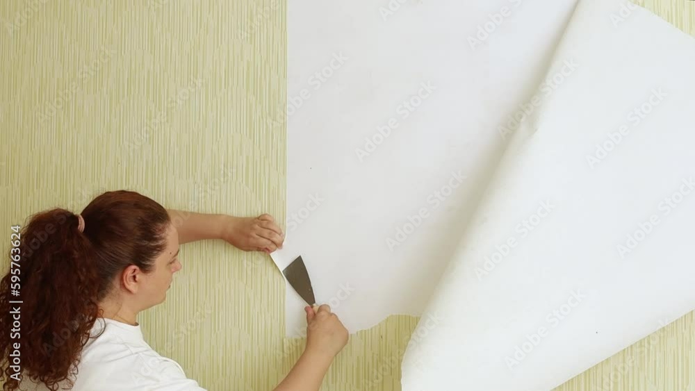 Curly red haired woman rip off old wallpaper with scraper and empty