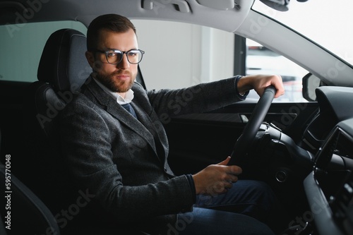 Handsome businessman driving car to airport, going on business side view, copy space. Happy man in stylish suit going to business meeting in the morning, driving his luxury car, shot from cabin. © Serhii