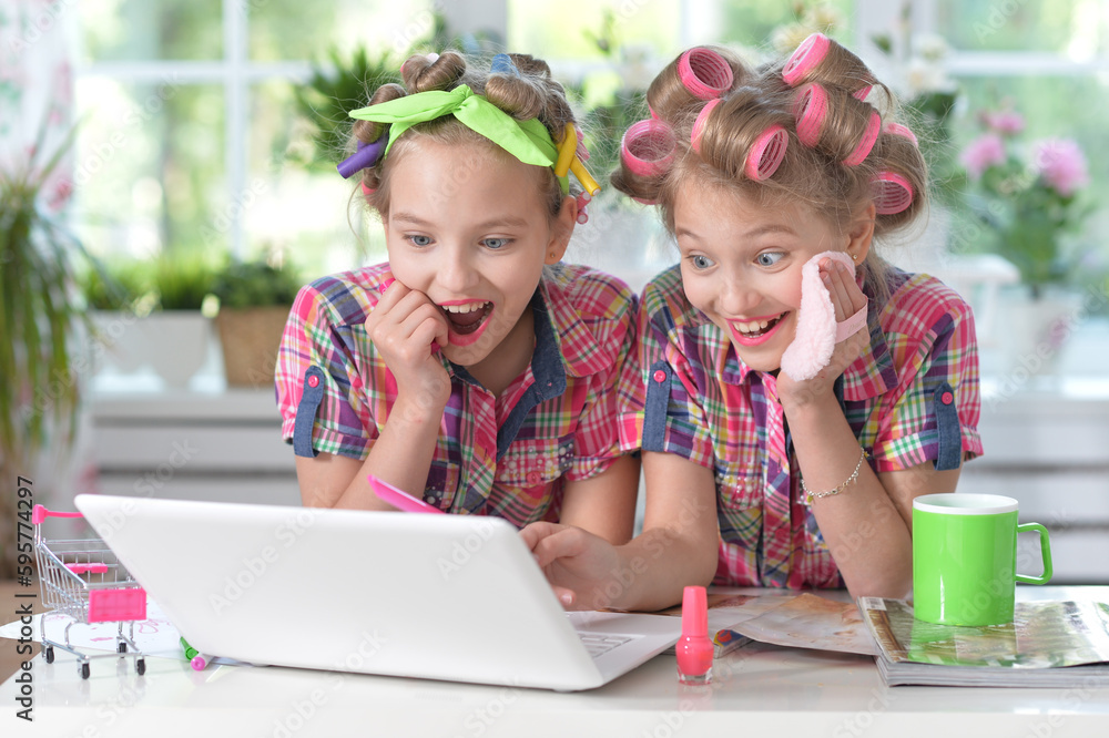 Cute twin girls in hair curlers with laptop at home Cute twin girls in hair curlers with laptop at home