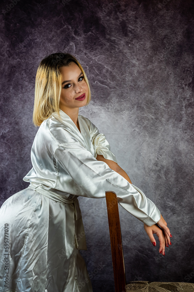 Obraz premium young slender blonde woman in a stylish dressing gown isolated on a beautiful background.