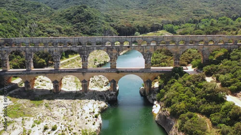 Tilted Aerial View of the Pont du Gard Aqueduct over the Hérault River, with a Canoe in the Background on a Summer Day in Occitanie Tilted Aerial View of the Pont du Gard Aqueduct over the Hérault River, with a Canoe in the Background on a Summer Day in Occitanie