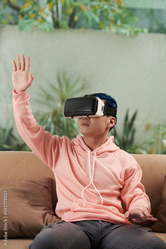 Obraz premium Young man in pink hoodie playing videogame in VR headset