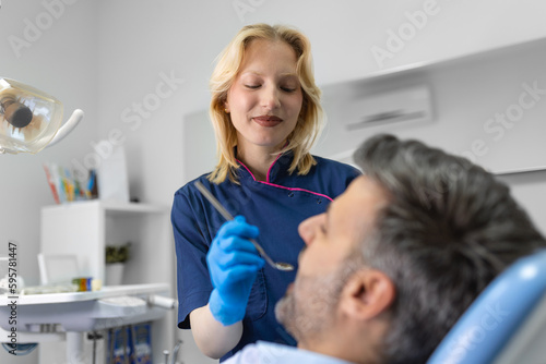 Female dentist curing teeth cavity in blue gloves. Dentist caries treatment at dental clinic office. People, medicine, stomatology and health care concept