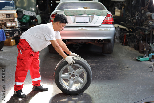 Man technician car mechanic in half uniform holding tire for replacement or changeing at repair garage. Happy asian worker smiling and looking at camera. Concept of car center repair service.