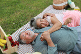 Top view happy asian senior man and woman lying on blanket and having fun on picnic together in garden outdoor. Lover couple eating food and embracing at the park. Happiness marriage lifestyle concept