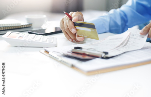 Asian businessman holding credit card to checking invoice and use calculator to calculate cost from online order, A man start new business online and using a credit card to pay for order