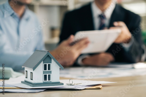 Real estate agent with client or architect team discussing project on an electronic tablet behind the home architectural model. Home Insurance and Real estate investment concept.