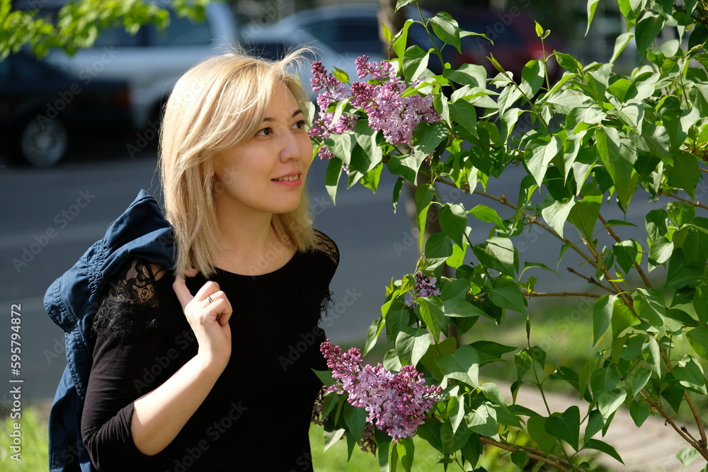 A young woman stands near a blooming lilac tree. A young woman stands near a blooming lilac tree.