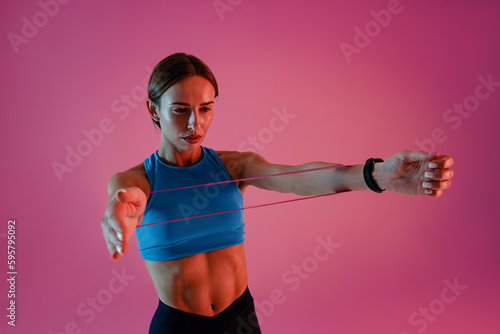 Woman performs fitness exercises with resistance band on studio background. High quality photo