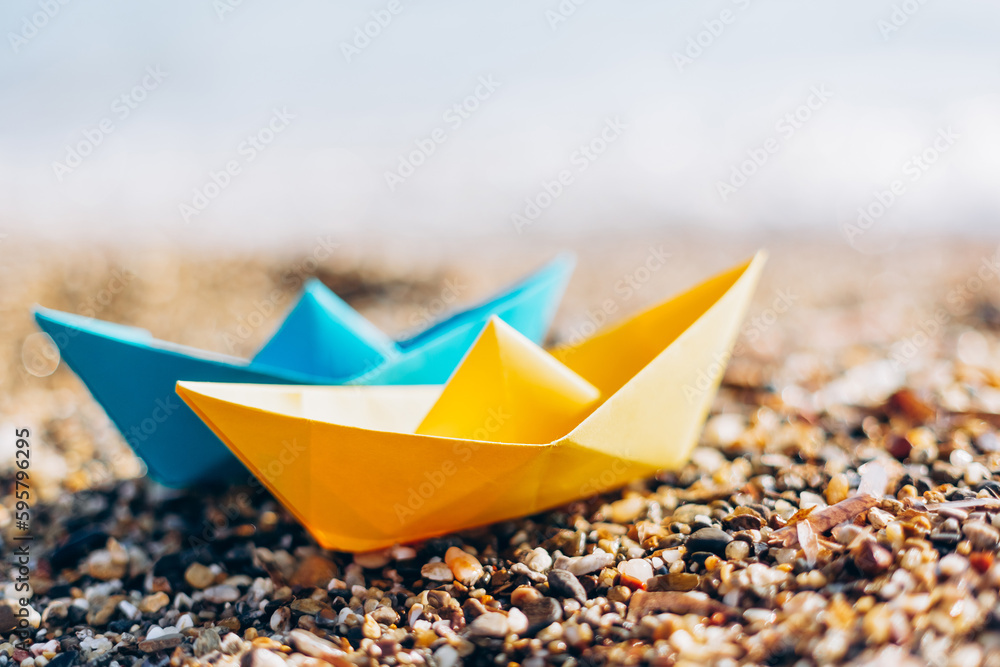 Blue and yellow paper boats on the pebble beach Blue and yellow paper boats on the pebble beach