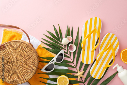 Stylish summer getaway concept. Top view flat lay of yellow striped flip-flops, towel, green palm leaves, vintage sunglasses, bag on pastel pink background with empty space for text or advert
