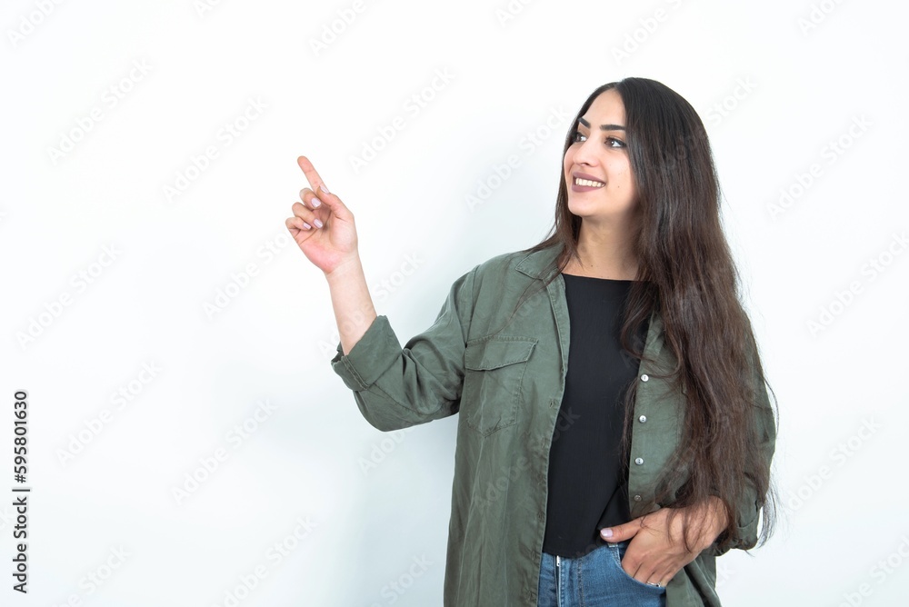 Smiling young brunette woman wearing casual clothes over white studio background indicating finger empty space showing best low prices Smiling young brunette woman wearing casual clothes over white studio background indicating finger empty space showing best low prices