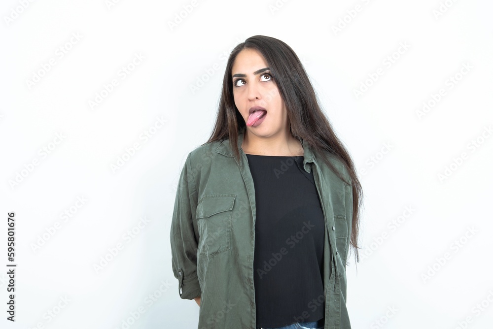 young brunette woman wearing casual clothes over white studio background showing grimace face crossing eyes and showing tongue. Being funny and crazy young brunette woman wearing casual clothes over white studio background showing grimace face crossing eyes and showing tongue. Being funny and crazy