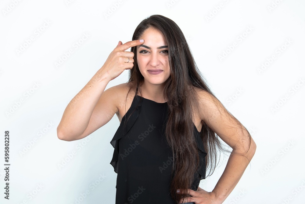 young brunette woman wearing black blouse over white studio background pointing unhappy at pimple on forehead, blackhead infection. Skincare concept. young brunette woman wearing black blouse over white studio background pointing unhappy at pimple on forehead, blackhead infection. Skincare concept.