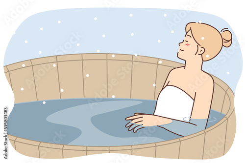 Woman relaxes in wooden finnish sauna pool with hot water enjoying warm outdoor spa